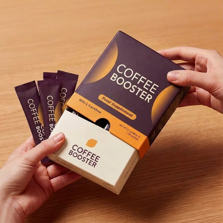 Geöffnete Coffee Booster Packung zwischen zwei Händen, pflaumenfarbene Beutel auf einem Holztisch