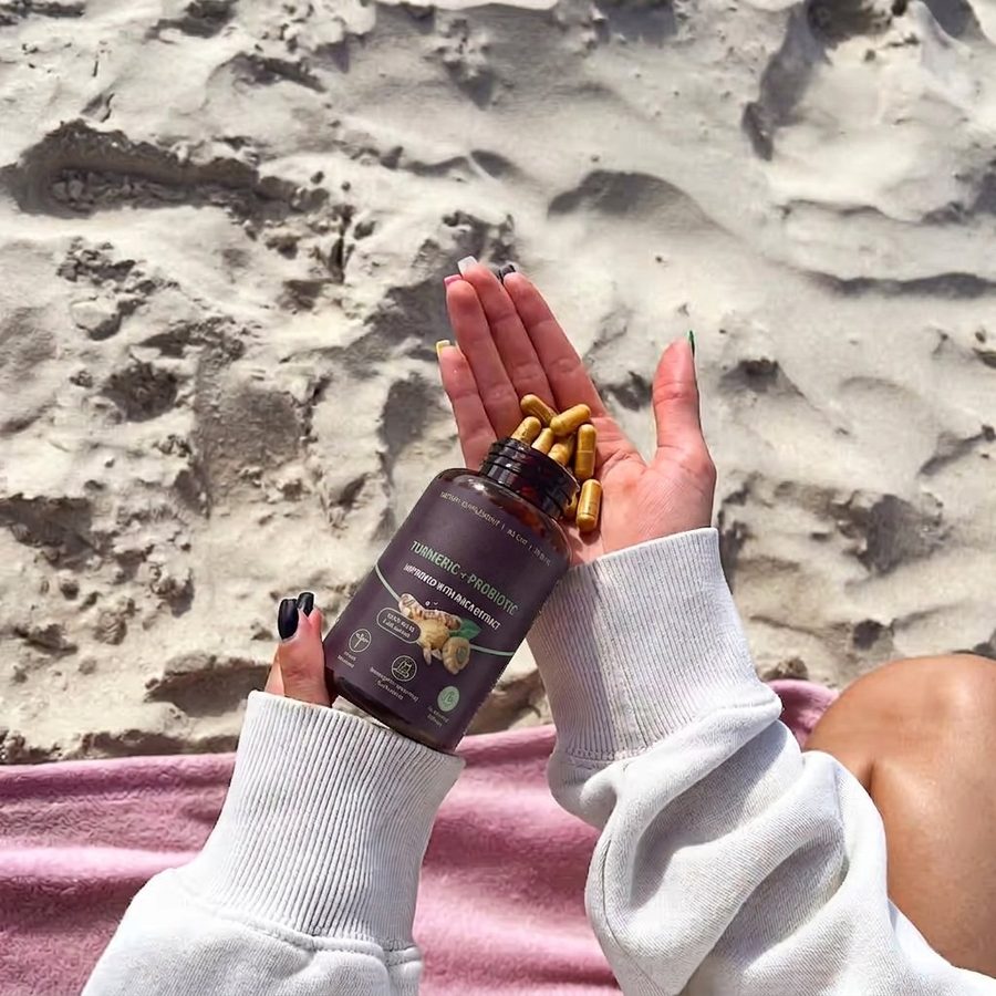 Flasche Turmeric + Probiotic über einer geöffneten Hand mit bernsteinfarbenen Kapseln